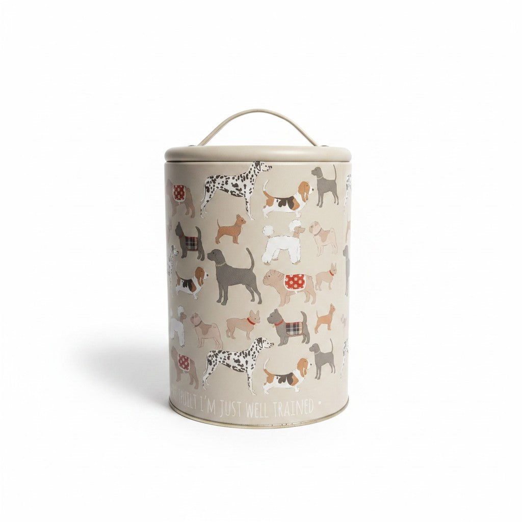 Une boîte de rangement cylindrique en métal de couleur beige crème, présentée de face sur un fond blanc neutre. La surface est décorée d'une multitude d'illustrations de différentes races de chiens (Dalmatien, Basset Hound, Caniche, Carlin) dans des tons marron, gris et blancs. La boîte est surmontée d'un couvercle équipé d'une poignée plate en métal.