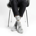 Chaussettes grises motifs chiens kawaii portées sur chaise blanche avec pantalon noir chaussettes fantaisie woof pour amoureux des chiens
