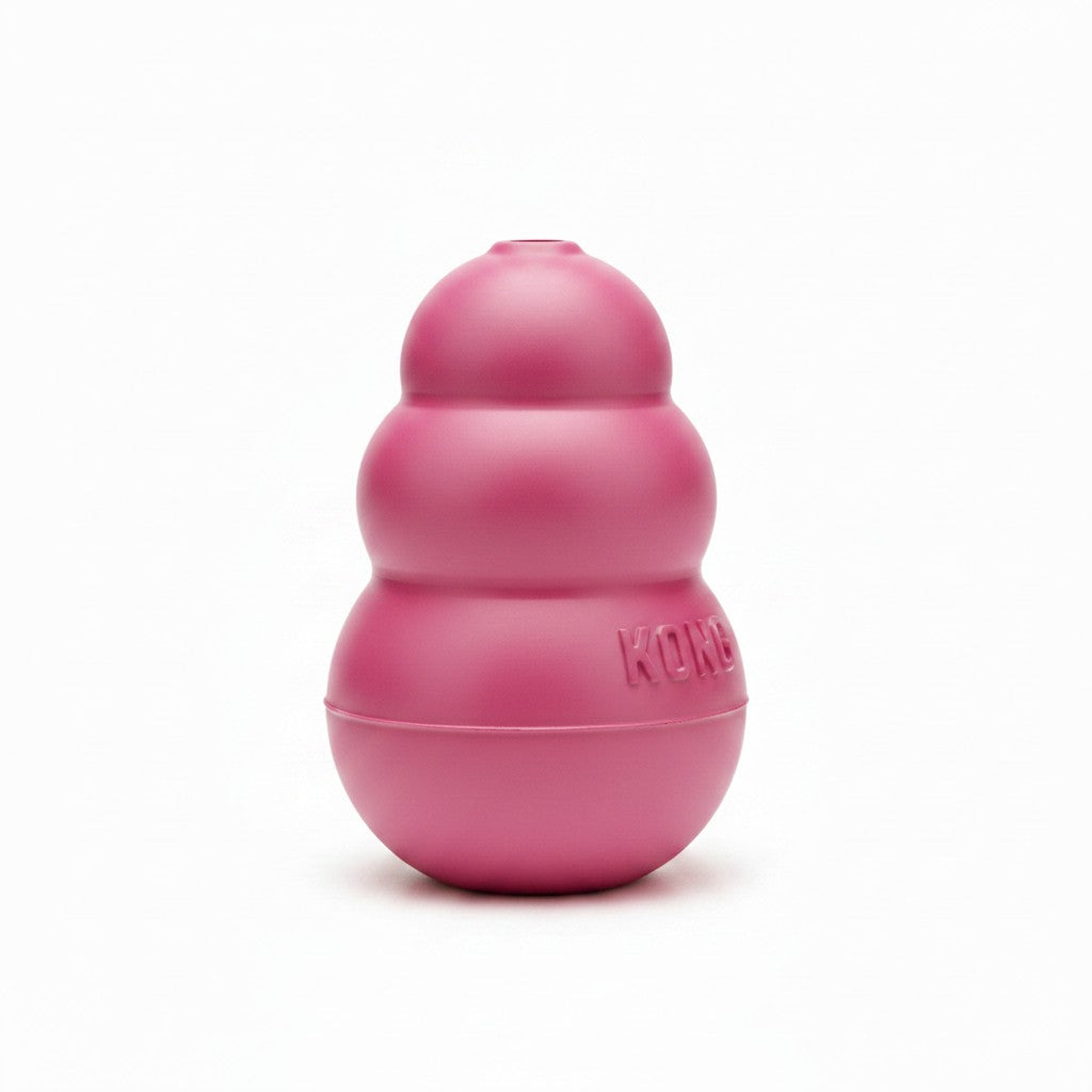 Jouet d'occupation KONG Puppy pour chiot en caoutchouc souple rose, présenté debout sur un fond blanc uni. L'objet a une forme conique emblématique composée de trois sphères superposées de taille décroissante, avec une ouverture au sommet. Le logo de la marque "KONG" est moulé en relief sur la base