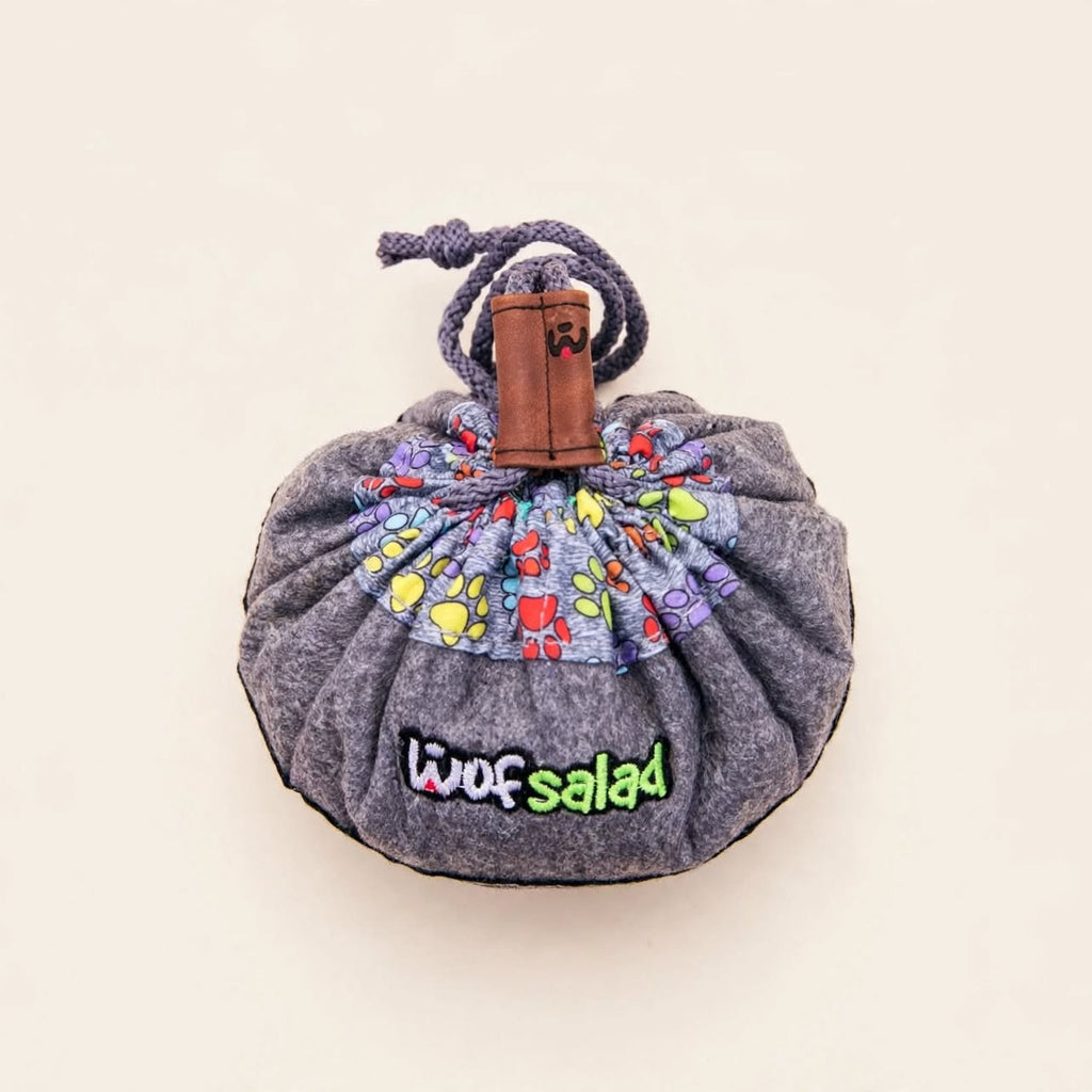 Pochette de rangement grise chinée à motif pattes multicolores, fermée par un cordon coulissant avec embout en cuir marron, marquée "Woof Salad"
