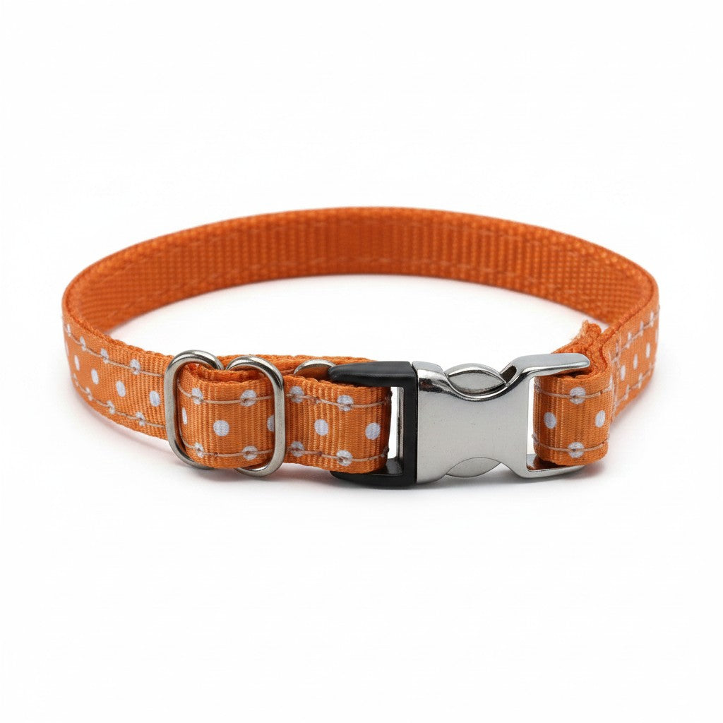 Un collier réglable pour chien, présenté fermé et photographié de face sur un fond blanc neutre. La sangle extérieure est d'une couleur orange vif, imprimée de motifs réguliers à pois blancs, tandis que la doublure intérieure est en nylon tissé orange uni. Le système de fermeture comprend une boucle rapide combinant du plastique noir et du métal argenté poli. Le collier intègre également un passant de réglage métallique double et un petit anneau en D en métal pour y fixer une laisse ou un médaillon.