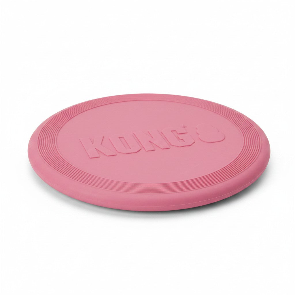 Frisbee souple pour chien en caoutchouc rose clair, présenté à plat et légèrement de biais sur un fond blanc uni. Le logo de la marque "KONG" est gravé en grandes lettres capitales en relief au centre du disque. Le bord extérieur est texturé avec plusieurs lignes circulaires concentriques.