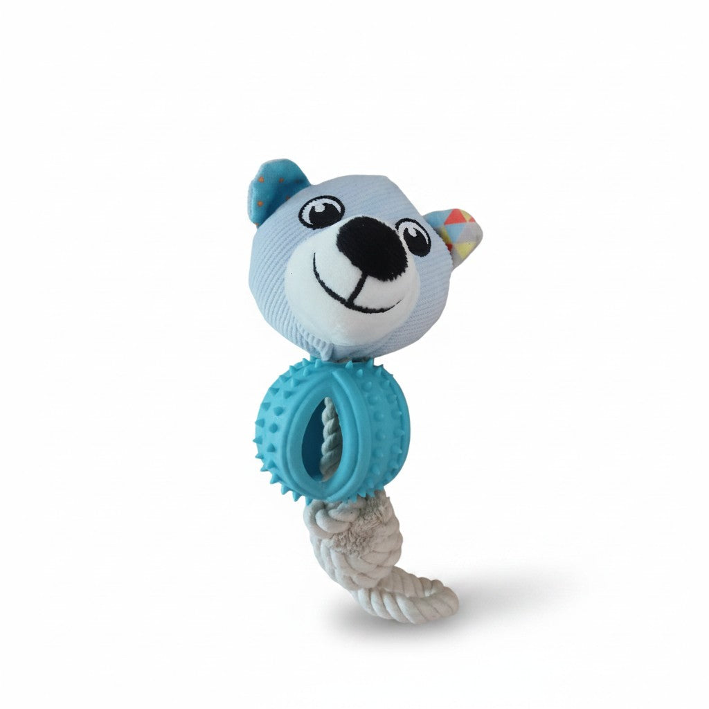 Un jouet pour chien composé d'une peluche en forme de tête d'ours bleu clair, reliée à une corde en coton blanc tressé. La corde traverse un anneau central épais en caoutchouc bleu turquoise recouvert de petits picots souples pour masser les gencives. La tête de l'ours présente des yeux et un sourire brodés en noir et blanc, avec l'intérieur d'une oreille à motifs colorés, le tout photographié de face sur un fond blanc uni.