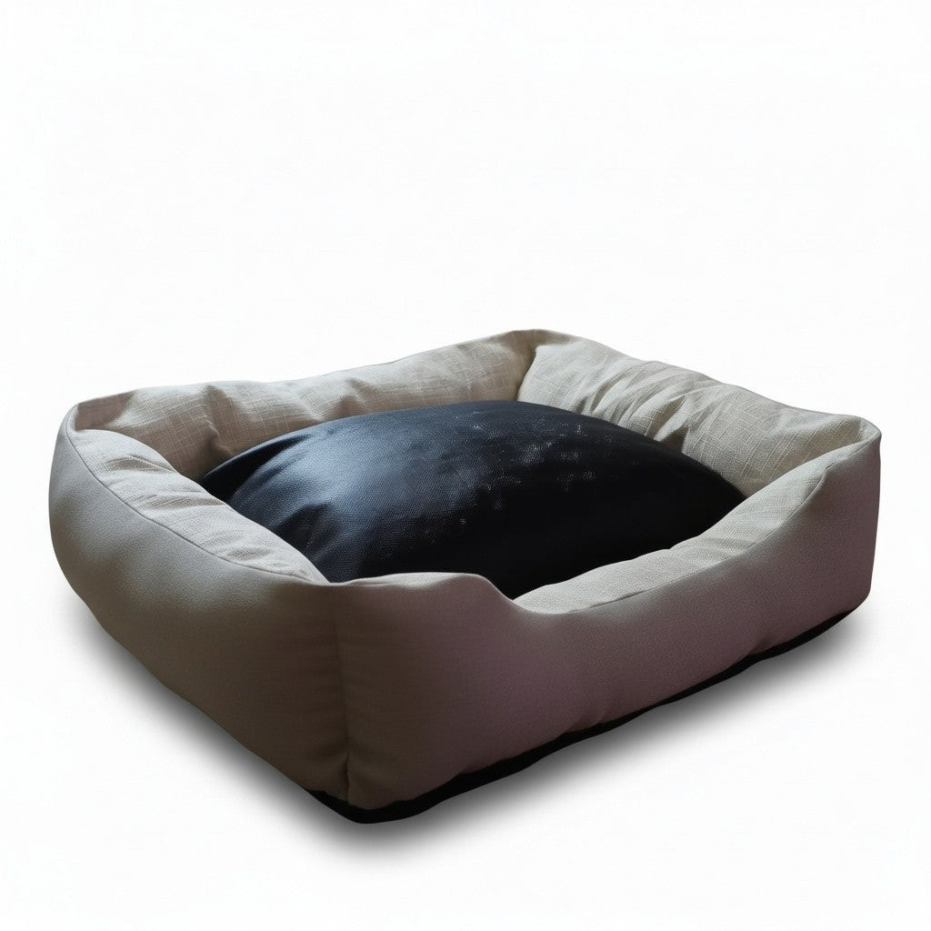 Un panier pour chien de forme rectangulaire, photographié de trois-quarts sur un fond blanc neutre. La structure extérieure et les rebords épais et rembourrés sont confectionnés dans un tissu texturé de couleur beige clair. Le centre du panier est occupé par un grand coussin noir bombé et lisse. Le dessous du panier est souligné par une base noire antidérapante.