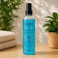 Flacon spray transparent de 250 ml de lotion lavante sans rinçage Aisance ANJU BEAUTÉ, contenant une lotion bleue et présenté sur une table en bois.