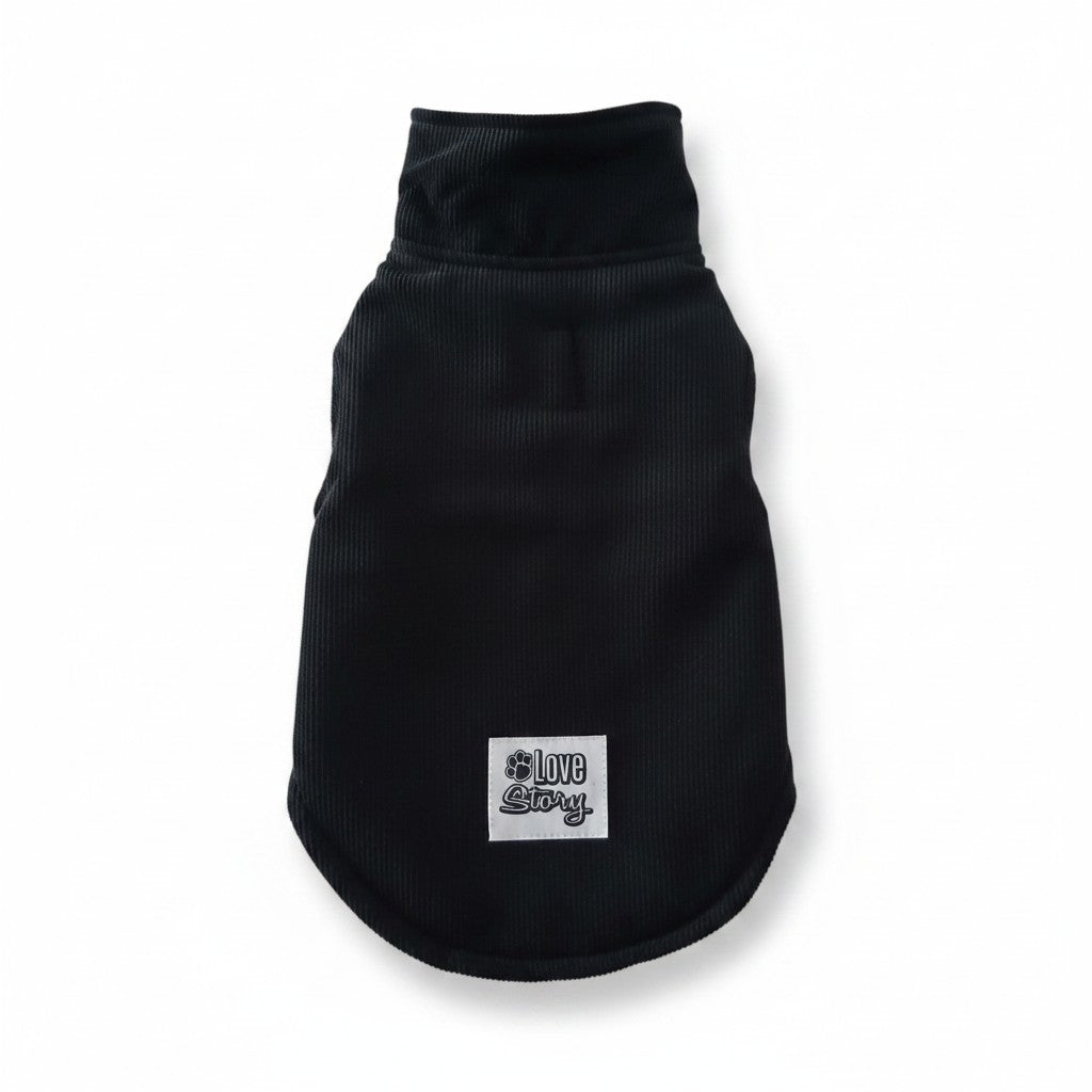 Manteau en velours côtelé noir pour chien, présenté de dos à plat sur fond blanc. Le vêtement possède un col montant épais et une petite fente verticale discrète au milieu du dos pour laisser passer l'attache de la laisse. Un écusson carré blanc avec la marque "Love Story" écrite en lettres stylisées noires est cousu sur le bas.