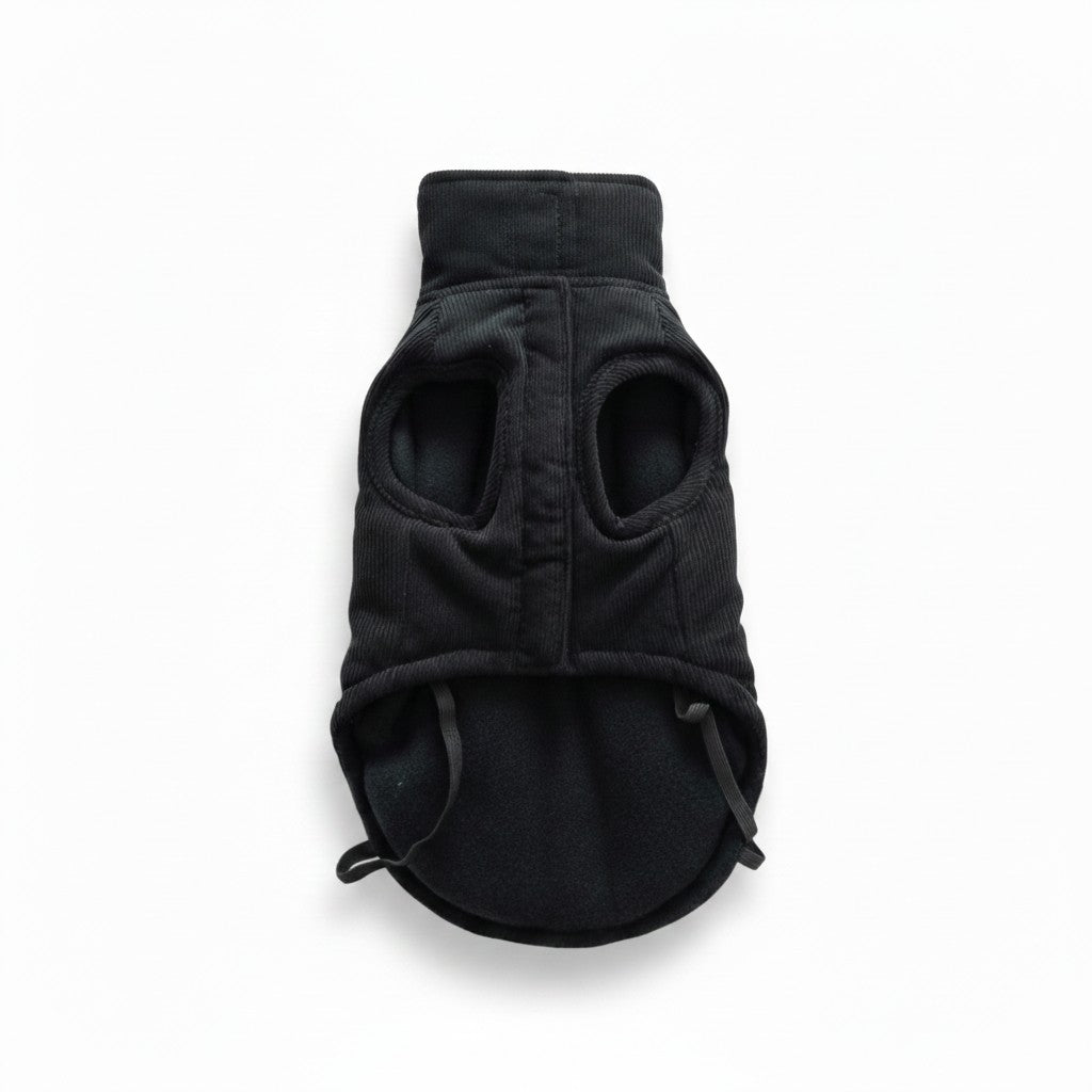 Vue de dessous du manteau en velours côtelé noir pour chien, disposé à plat sur fond blanc. La fermeture ventrale centrale s'effectue par une bande velcro dissimulée sous un rabat. L'intérieur révèle une doublure en polaire noire douce, deux emmanchures et deux élastiques fins à l'arrière pour maintenir les pattes arrière du chien.