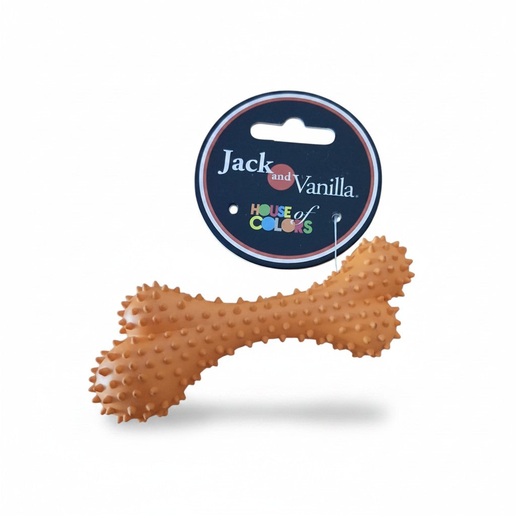 Jouet pour chien en forme d'os orange clair de la marque Jack and Vanilla, présenté sur fond blanc. L'os en caoutchouc souple est entièrement recouvert de petits picots souples en relief pour masser les gencives. Une étiquette cartonnée ronde et noire est fixée au sommet, affichant la marque "Jack and Vanilla" et la collection "House of Colors".