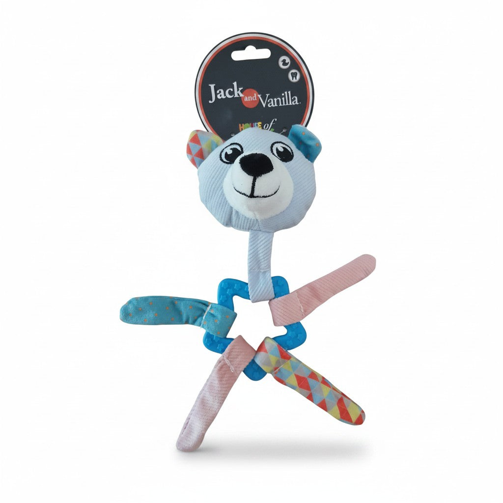 Un jouet d'éveil pour chiot de la marque Jack and Vanilla, associant une peluche en forme de tête d'ours bleu clair à un anneau de dentition texturé en plastique souple bleu. La tête du personnage, aux détails brodés noirs et blancs, surmonte un anneau en forme d'étoile auquel sont noués quatre rubans de tissu colorés aux motifs variés (rose pâle, bleu à pois, motifs géométriques multicolores). Présenté sur un fond blanc neutre, le produit conserve son étiquette d'emballage d'origine en carton noir et rouge
