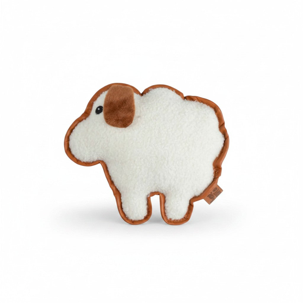 Peluche plate pour chien en forme de mouton, présentée de profil sur un fond blanc uni. Le jouet possède un corps blanc en fausse fourrure sherpa bouclée, une petite oreille marron en peluche douce et un œil noir brodé. Tout le contour de la silhouette est souligné par un liseré en tissu marron, et une petite étiquette de la marque dépasse sur le bas droit.