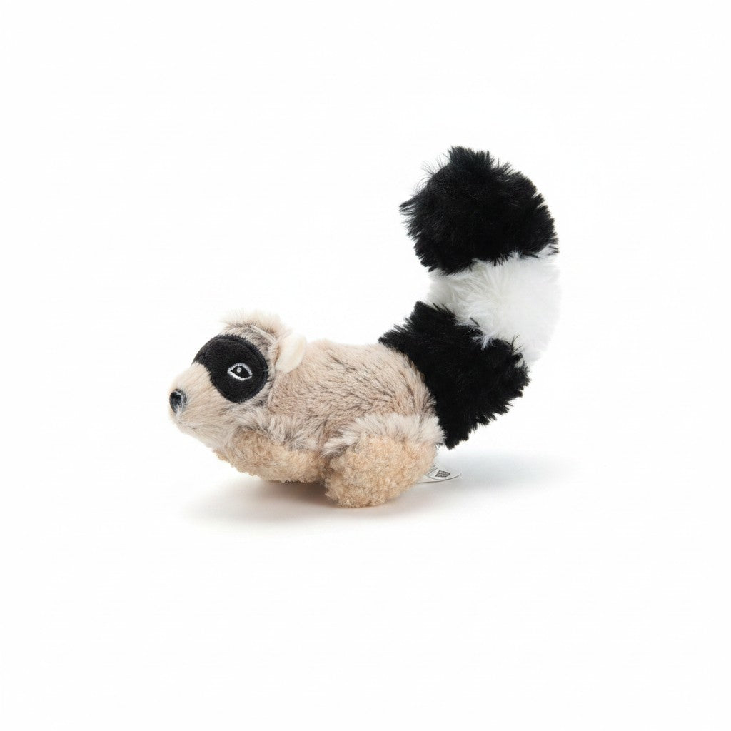 Un jouet en peluche pour chien représentant un petit raton laveur. Le corps de l'animal est recouvert d'une fourrure synthétique rase de couleur beige et marron clair, avec un masque noir brodé autour des yeux et une truffe noire. Sa longue queue touffue et dressée présente des anneaux alternant le noir et le blanc. L'objet est photographié de profil sur un fond blanc épuré.