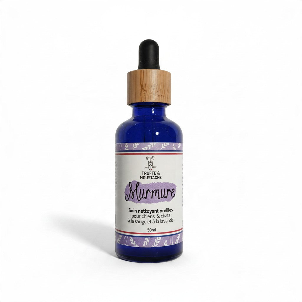 Flacon en verre bleu avec compte-gouttes noir et bague en bambou, étiquette violette tricolore Murmure de la marque Truffe & Moustache, soin nettoyant oreilles pour chiens et chats à la sauge et à la lavande, 50 ml